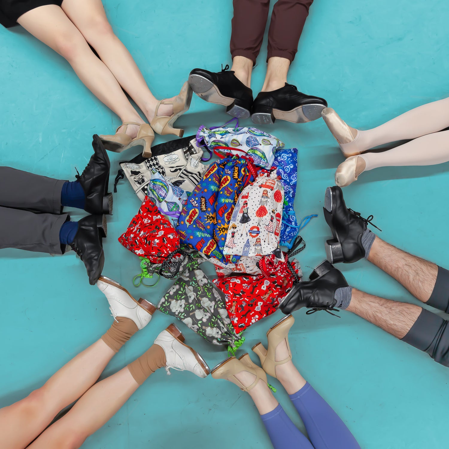 Dancers wearing a variety of dance shoes, sitting in a circle around a pile of colorful fabric shoe bags