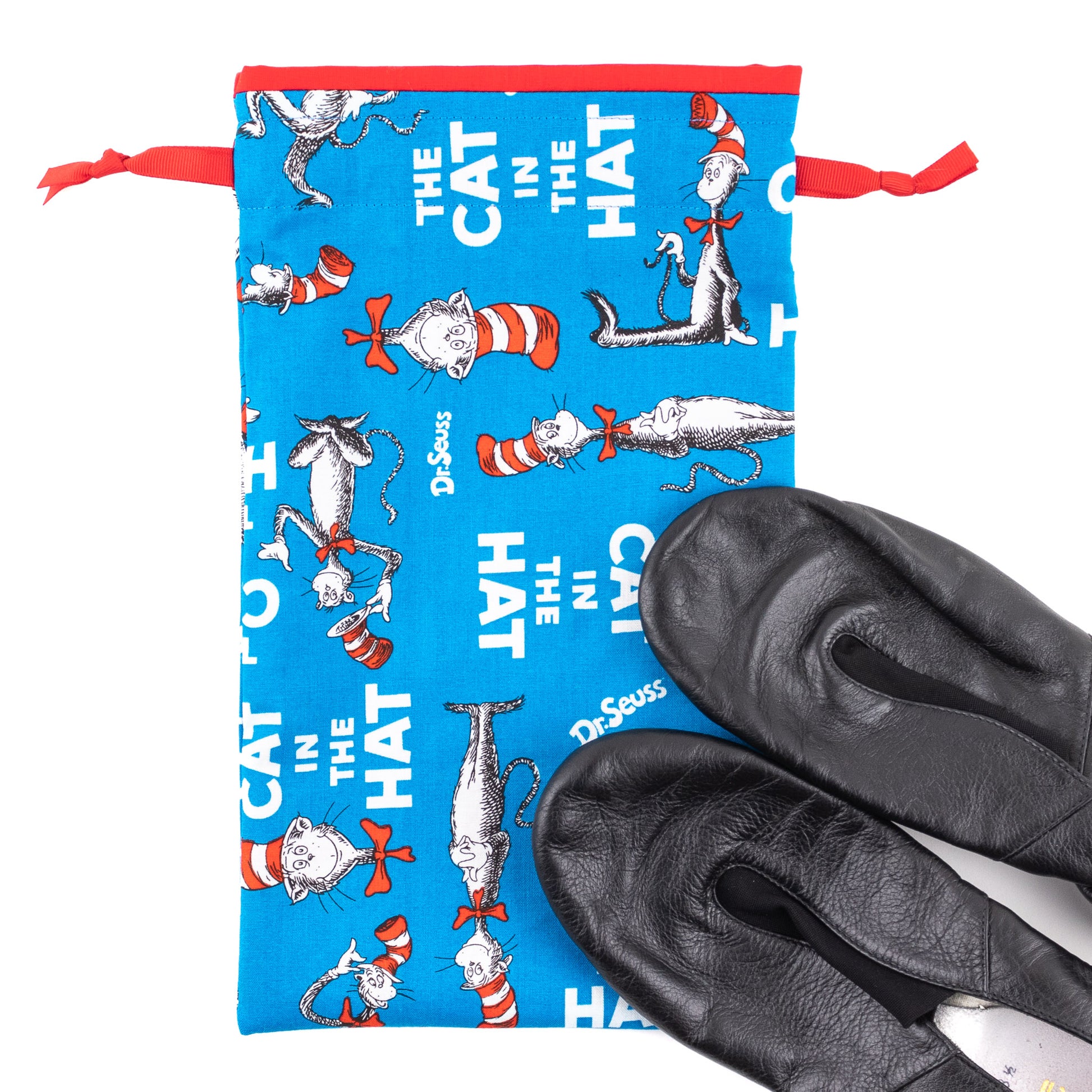 A pair of black jazz dance shoes next to a blue, red, and white cat-in-the-hat themed shoe bag