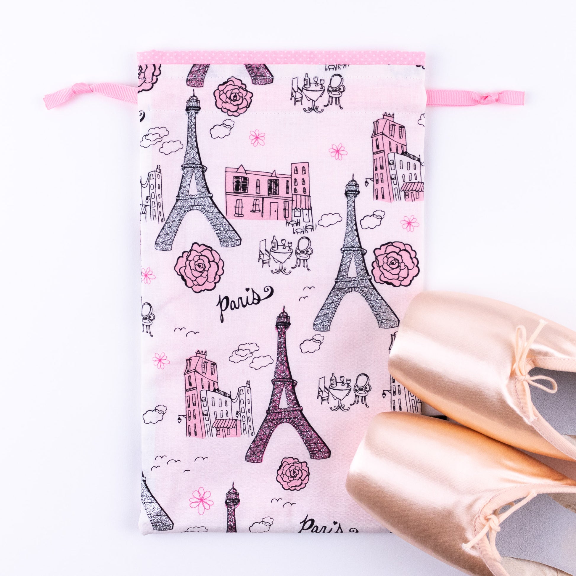 A pair of pink pointe ballet dance shoes next to a pink and white Paris themed shoe bag