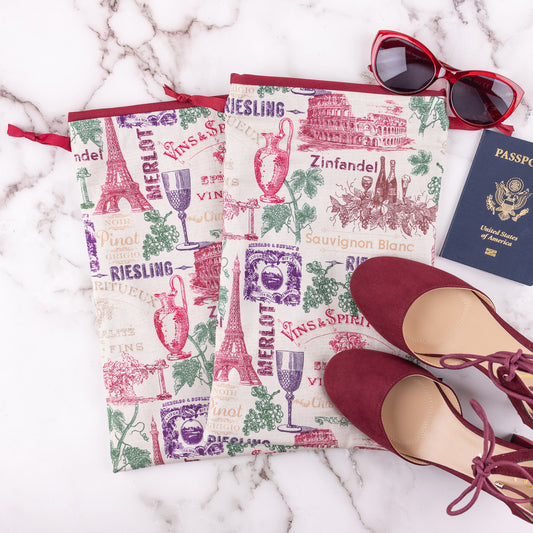 Set of two travel shoe bags in European wine themed fabric with red sunglasses, red shoes, and passport